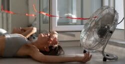 Woman lying on the floor in front of a fan because her AC is broken